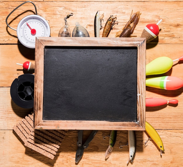 An overhead view of blank wooden slate over the fishing equipment on wooden desk