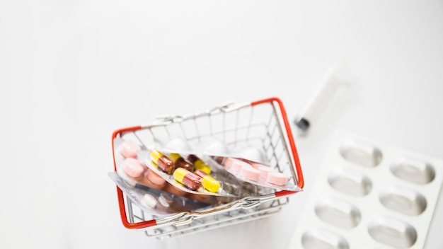 Overhead view of blister pills in shopping cart on white background