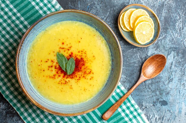 Overhead view of a blue pot with tasty soup served with mint and pepper next to chopped lemon wooden spoon on blue background