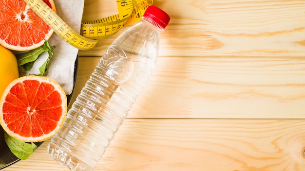 Overhead view of bottle; measuring tape and citrus fruits on wooden background