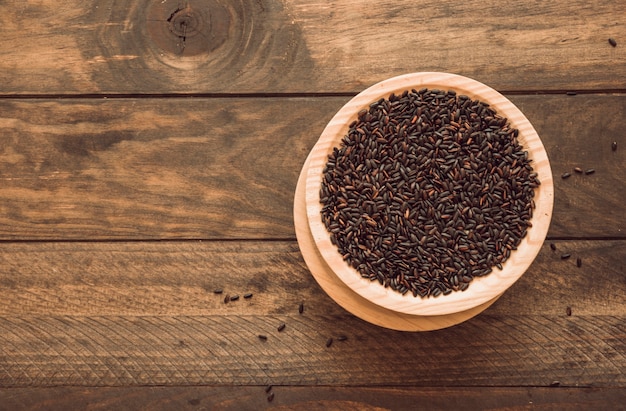 Overhead view of bowl with black rice grain on wooden background