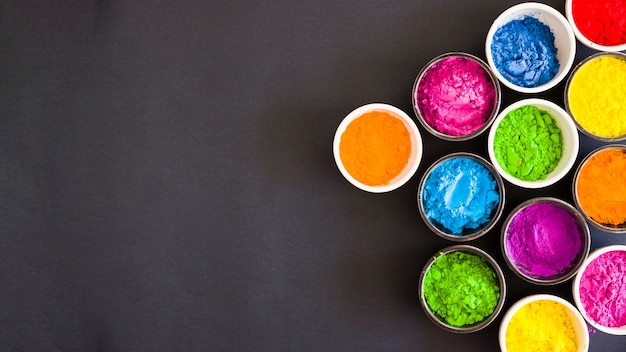 An overhead view of bowls with color holi powder on black backdrop