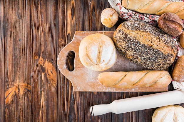 Верхний вид хлебных хлебов на разделочной доске над деревянным столом