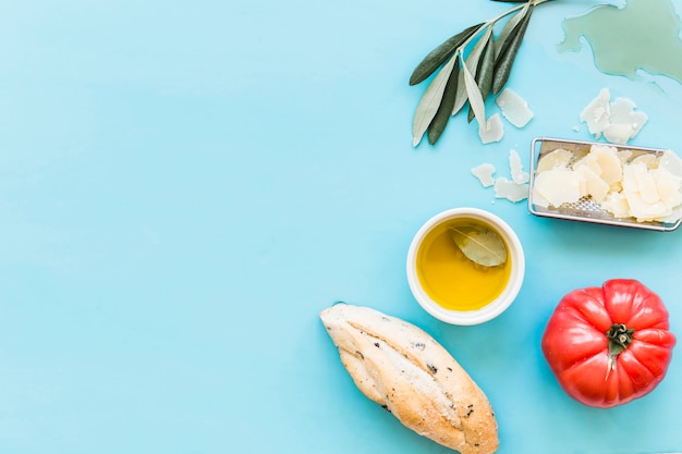 Overhead view of bread, oil, grated cheese and tomato on blue background