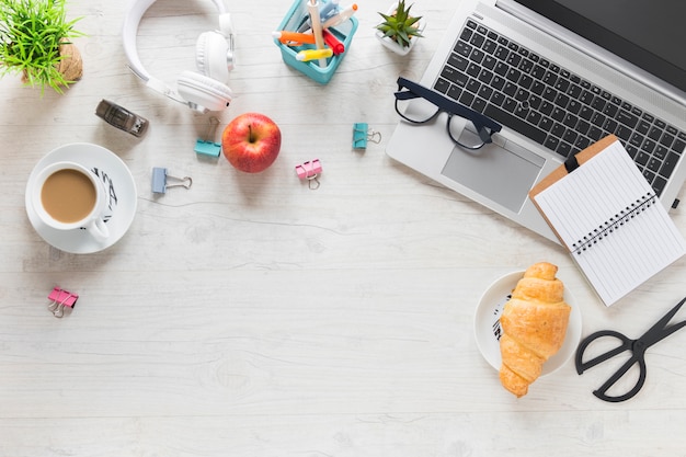 An overhead view of breakfast with office supplies and laptop on wooden desk
