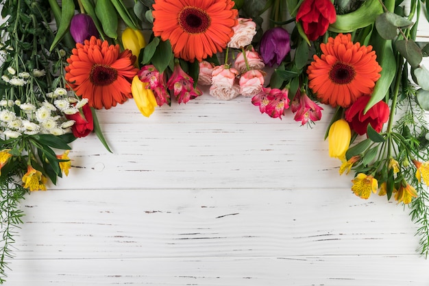 An overhead view of bright colored flowers on white wooden table