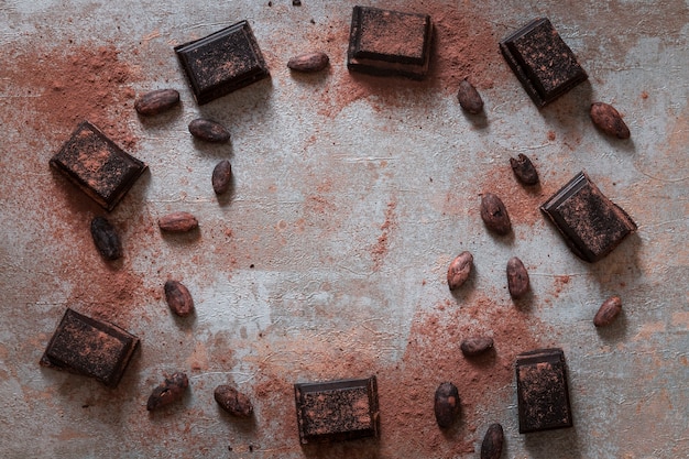 Overhead view of broken chocolate bas with cocoa powder and raw beans