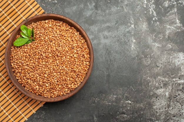 Overhead view of buckwheat groats with green in a brown bowl on brown tray on gray background