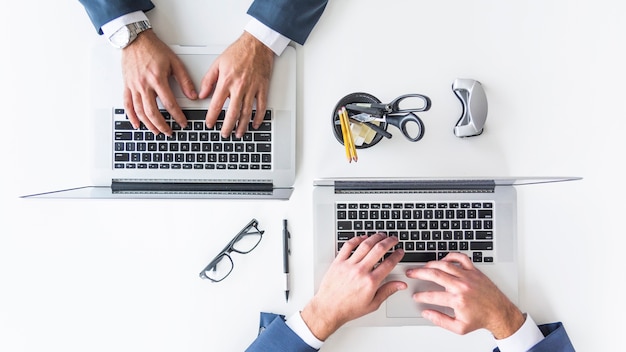 An overhead view of businessman's hand typing on laptop over white table top