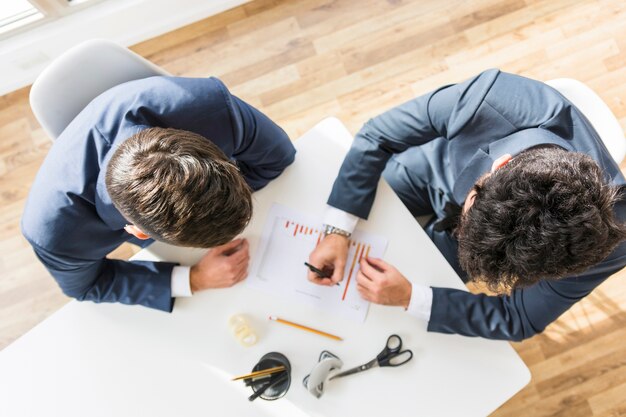 An overhead view of businessmen working on company financial report over the white desk