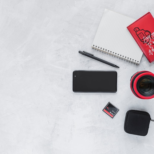 Overhead view of camera lens with cellphone, pen and notebook