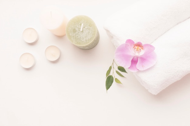 Overhead view of candle with orchid flower over the rolled up towel