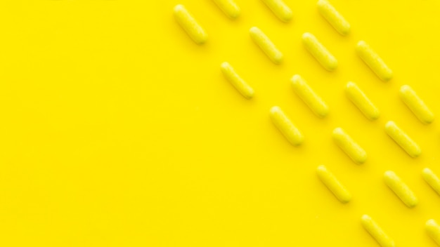 Overhead view of candy capsules in a row on yellow backdrop
