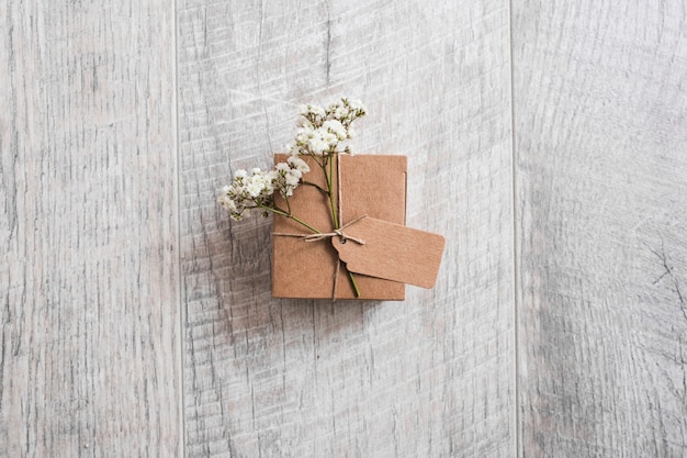An overhead view of cardboard box tied with tag and baby's-breath flowers on wooden desk