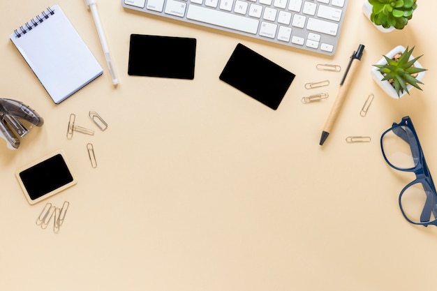 An overhead view of cards; spiral notepad; pen; eyeglasses and cactus plant with keyboard