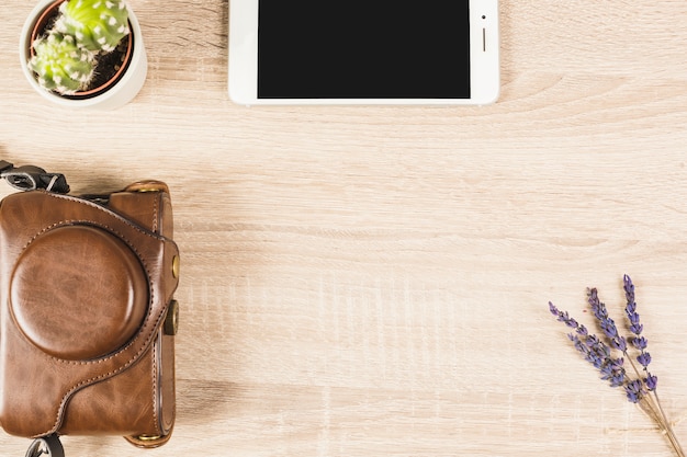 An overhead view of cell phone; cactus pot; lavender and camera in pouch on wooden background