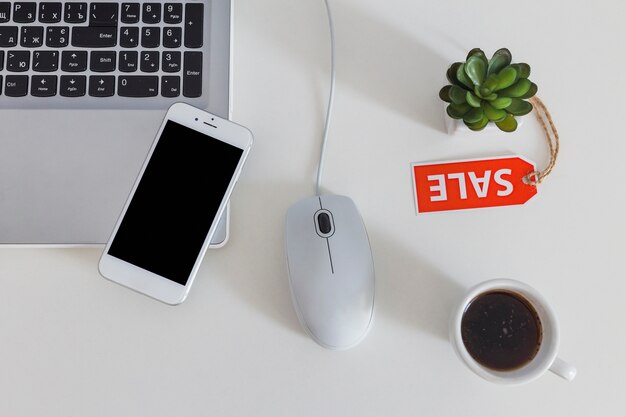 Overhead view of cellphone on laptop with sale tag and coffee on white table