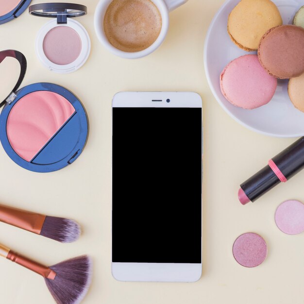 An overhead view of cellphone with cosmetics product and breakfast on beige background