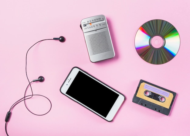 An overhead view of cellphone with earphone; cd; radio and cassette on pink background