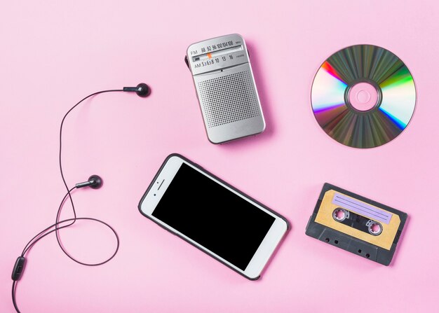 Вид сверху сотового телефона с наушником; CD; радио и кассеты на розовом фоне