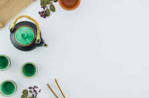 Free photo an overhead view of ceramic green herbal teapot and cups with herbs isolated on white background