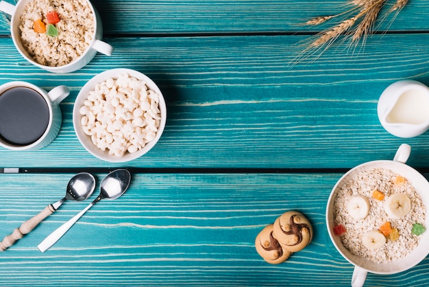 Overhead view of cereals, oatmeal with coffee and tea on turquoise table