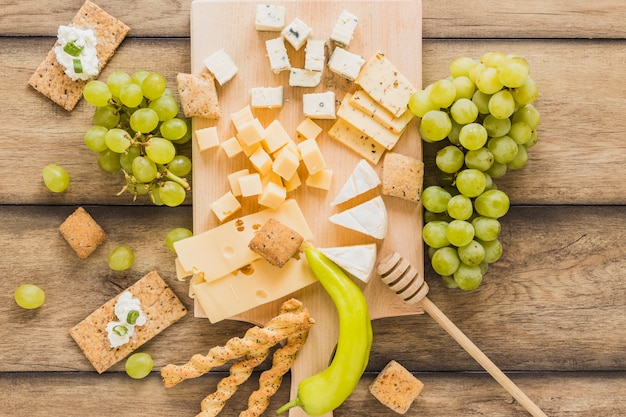 An overhead view of cheese blocks, grapes, crisp bread with cheese cream; green chili on wooden table