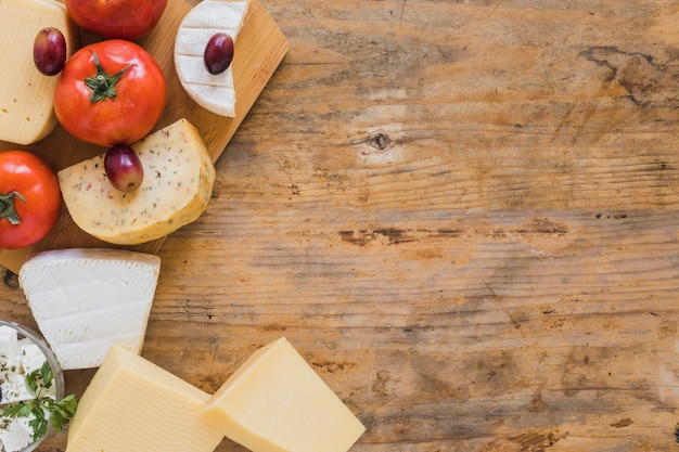 Free photo an overhead view of cheese blocks, grapes and tomatoes on wooden desk