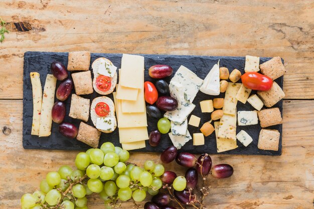 An overhead view of cheese, grapes and mini bread on slate board over the table