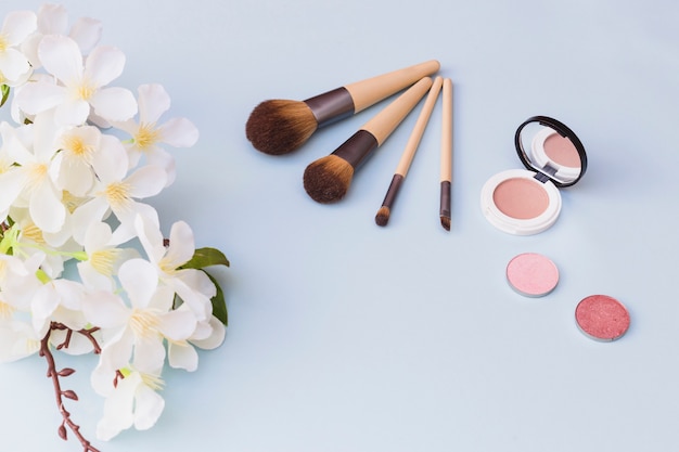 An overhead view of cherry blossom twig; makeup brush; blusher on blue background