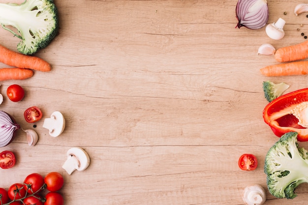 An overhead view of cherry tomatoes; mushroom; carrot; broccoli; garlic and bell pepper on wooden table with copy space for writing the text