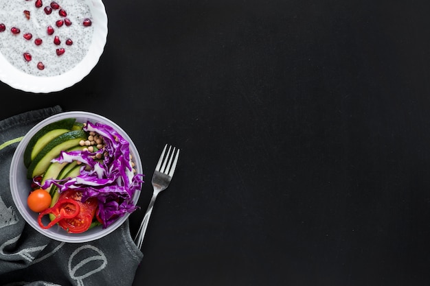 An overhead view of chia seed pudding and fresh vegetables salad over black background