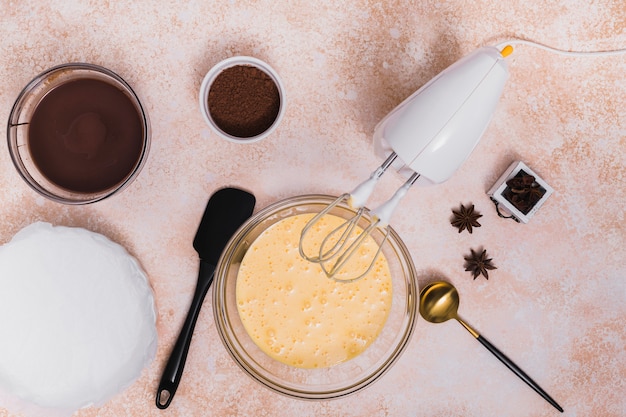 An overhead view of chocolate syrup; cocoa powder; anise; spatula; ladle and electric mixer on textured background