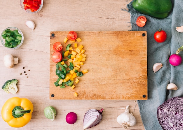 An overhead view of chopping board with chopped vegetables on wooden table