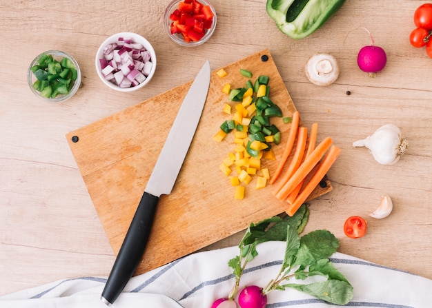 Free photo an overhead view of chopping board with knife and vegetables on wooden desk