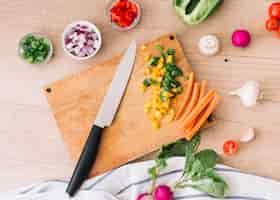 Free photo an overhead view of chopping board with knife and vegetables on wooden desk