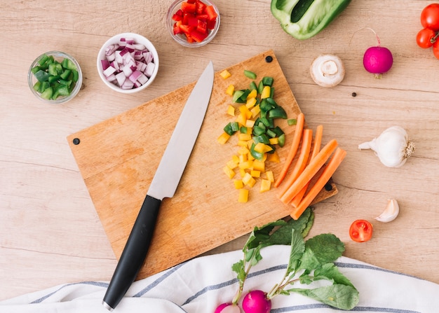 An overhead view of chopping board with knife and vegetables on wooden desk