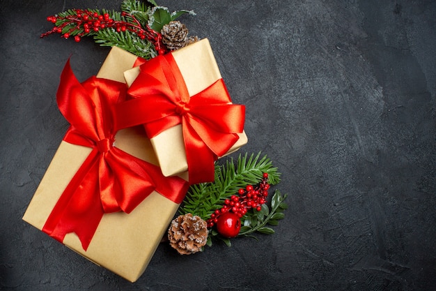 Vista dall'alto dell'atmosfera natalizia con bellissimi regali con nastro a forma di fiocco e accessori per la decorazione di rami di abete sul lato destro su uno sfondo scuro
