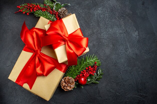 Вид сверху на рождественское настроение с красивыми подарками с бантом и украшениями из еловых веток справа на темном фоне