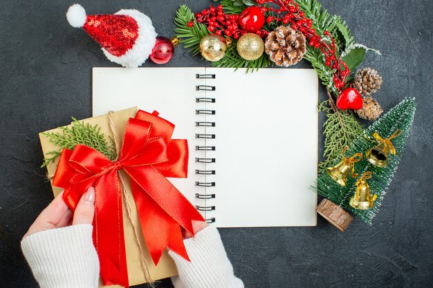 Overhead view of christmas mood with fir branches santa claus hat xsmas tree red ribbon on notebook on dark background