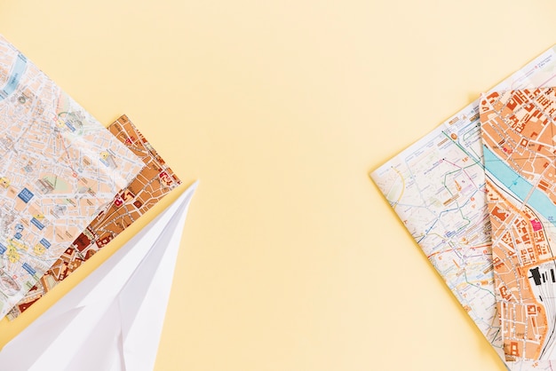 Free photo an overhead view of cities road maps and paper airplane on colored background