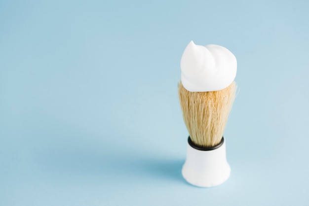 An overhead view of classic shaving brush with white foam against blue background