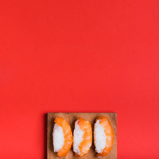 An overhead view of classic sushi with salmon on chopping board against red background