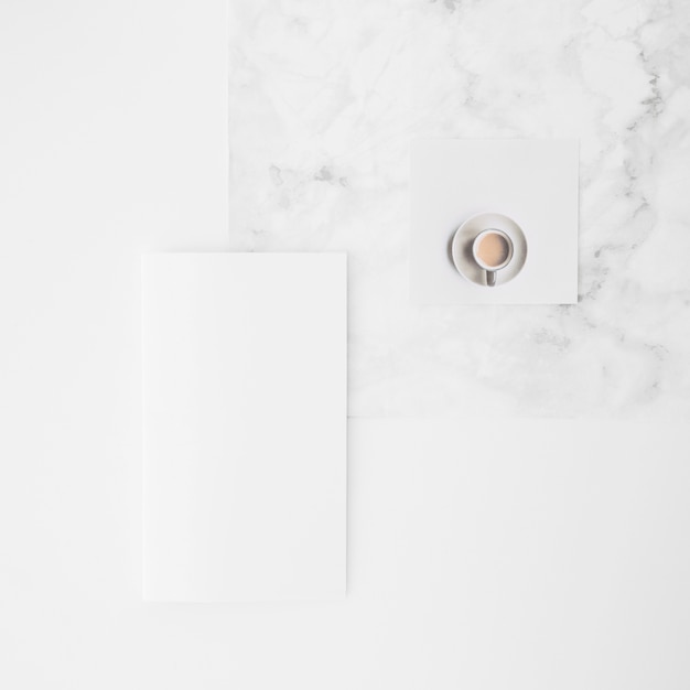 An overhead view of coffee cup and blank paper on desk against white background