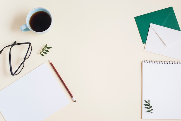 an overhead view of coffee cup; eyeglasses and stationeries on beige backdrop