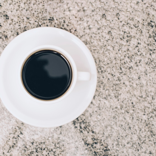 An overhead view of coffee cup and saucer on marble textured backdrop