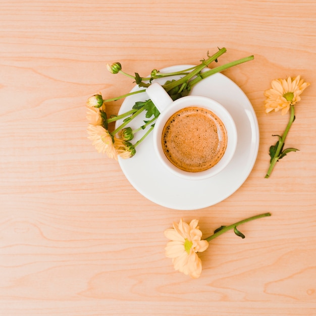 An overhead view of coffee cup and saucer with peach colored flowers on wooden textured background
