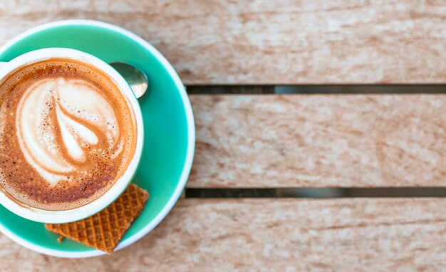 An overhead view of coffee cup with heart latte art on wooden table