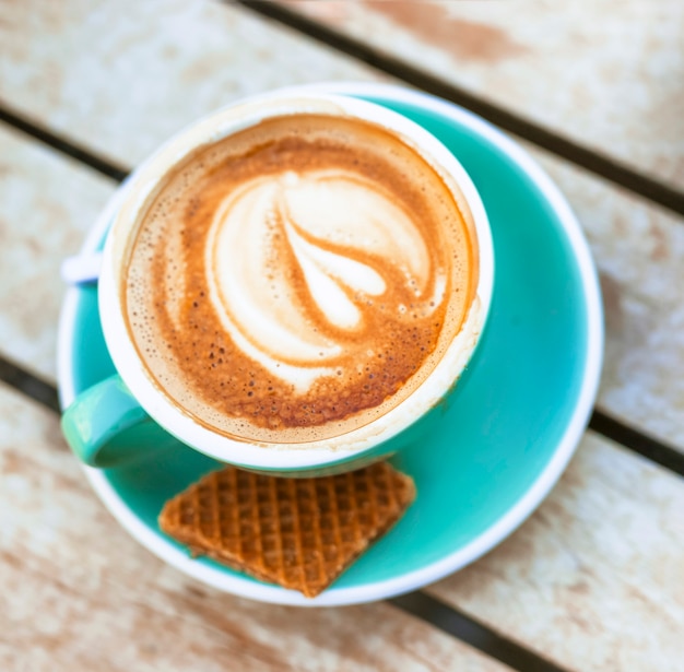 An overhead view of coffee cup with heart shape latte art and waffle