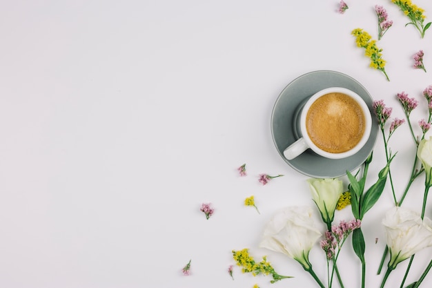 An overhead view of coffee cup with limonium; eustoma and goldenrods on white background